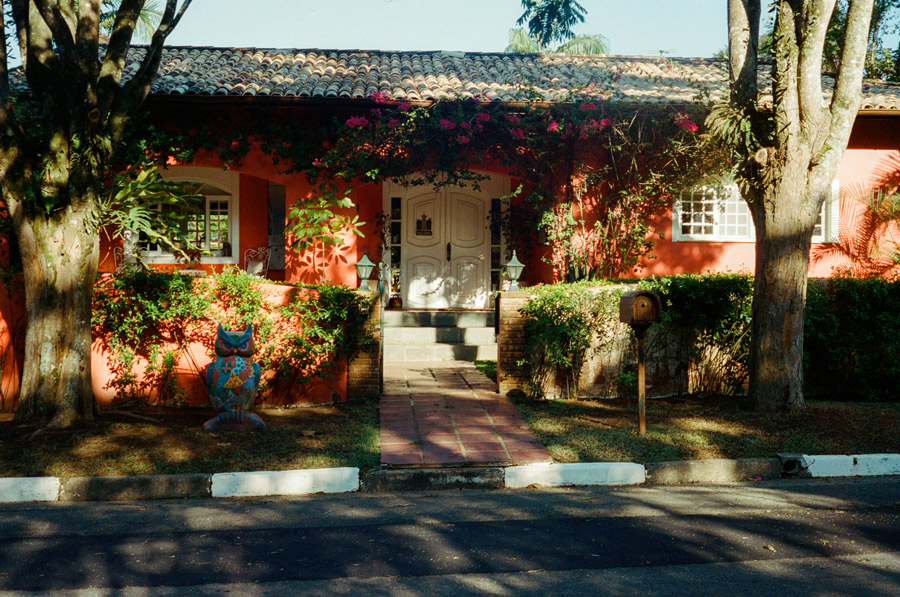 Fachada de residência tradicional, com jardim em frente, portas e janelas brancas de madeira.