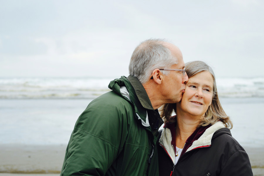 Casal de idosos na praia, homem beija mulher no rosto.